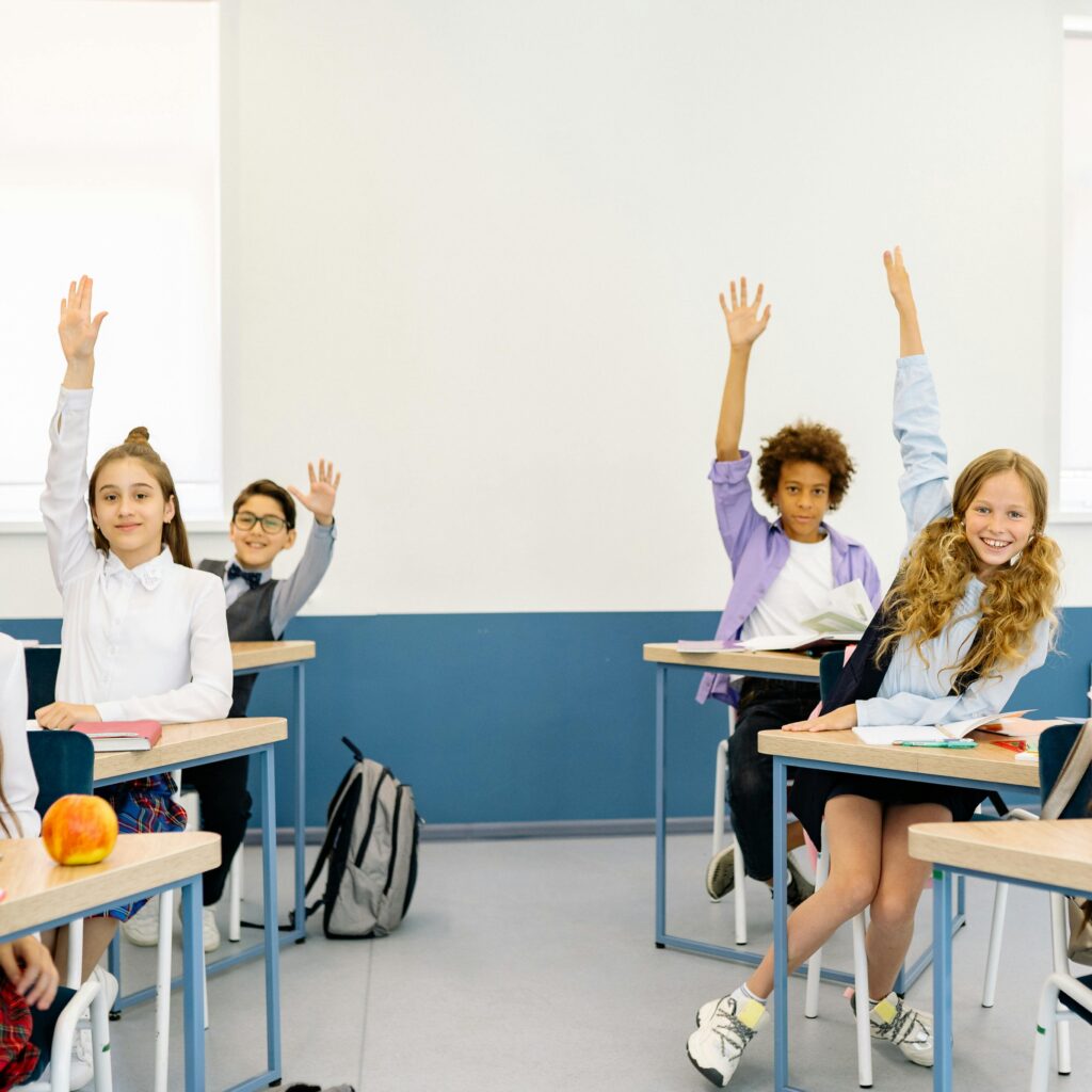 Students engaged in learning, raising hands in a bright classroom setting.