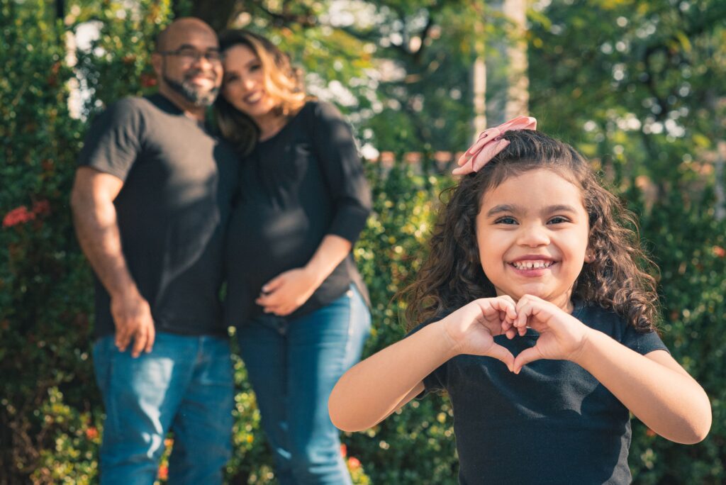 A joyful family in the park with a little girl and her expecting parents enjoying a sunny day.